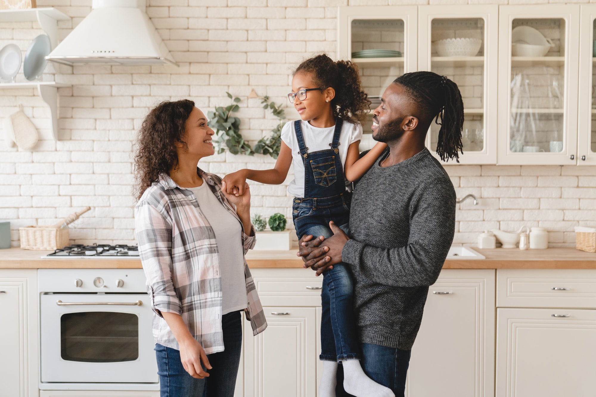 Parents holding daughter at home kitchen. Adoption and parenthood. Homeowners. Real estate